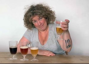 Nainen pitelee olut-lasia. Kolme lasia pöydällä