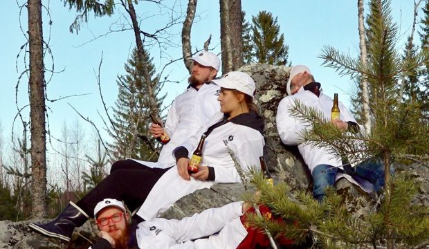 KUvassa neljä ihmistä metsässä valoiset takit päällä ja olutpullot käsissä