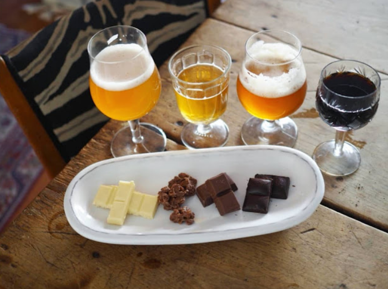 Erilaisia oluita erilaisissa laseissa ja lautasella erilaisia suklaita