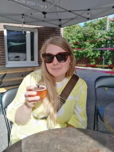 Nainen hymyilee kameralle kädessään lasillinen IPA-olutta