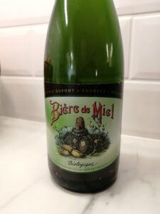Vihreä 0,75 litran olutpullo, jonka etiketissä oluttynnyreitä ja mehiläispesiä sekä teksti Bière de Miel